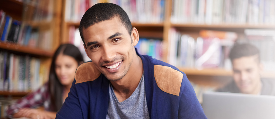 Junger arabischer Student sitzt in einer Bibliothek und lächelt in die Kamera