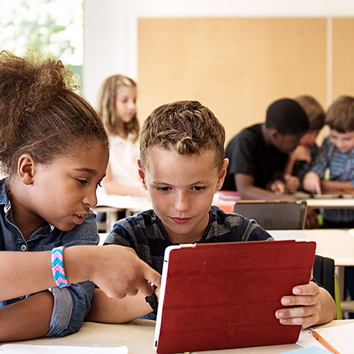 Grundschüler sitzen im Unterricht und arbeiten mit einem Tablet.