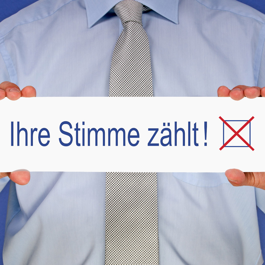 Ein Mann mit Krawatte und Hemd hält ein Schild mit der Aufschrift Ihre Stimme zählt und einem Kreuzchen vor sich. 