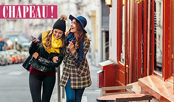 Zwei Frauen gehen Arm in Arm lachend an einem Pariser Cafe vorbei